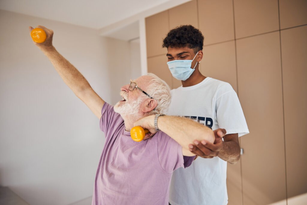 Senior man lifting weights supported by an instructor